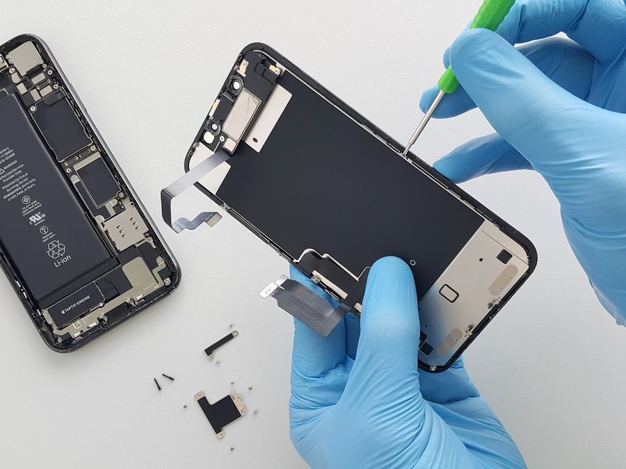 Manos con guantes retirando el módulo de pantalla de un celular